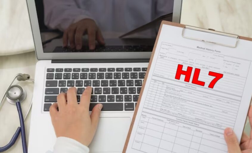 a doctor using a laptop while holding a clipboard that says “HL7”