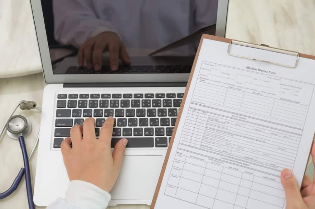 Close-up of hands typing near a medical history form and stethoscope