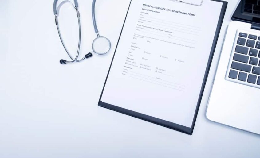 A stethoscope and medical form next to a laptop on a white surface