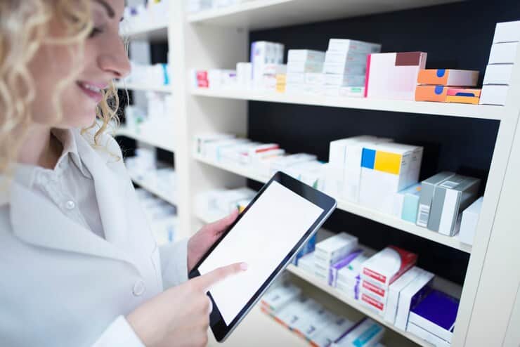 Pharmacist Holding Tablet by the Shelf Full of Medicine